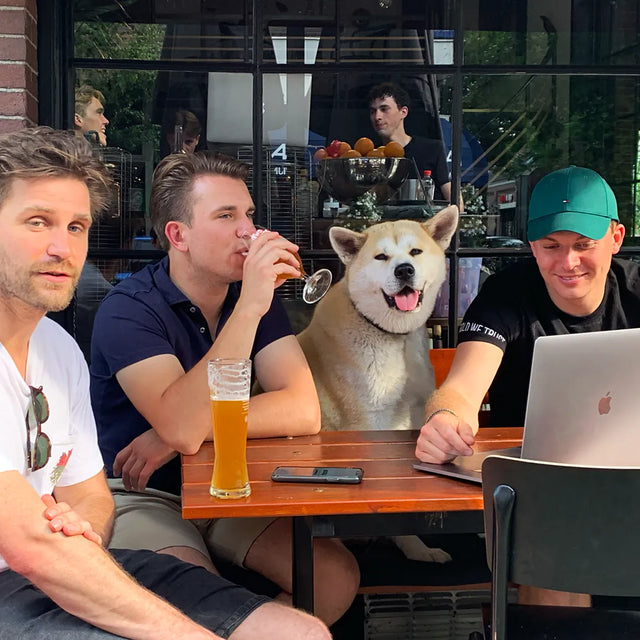Large dog sitting at an outdoor bar patio table with three men drinking beer; one man uses a laptop, in Amsterdam