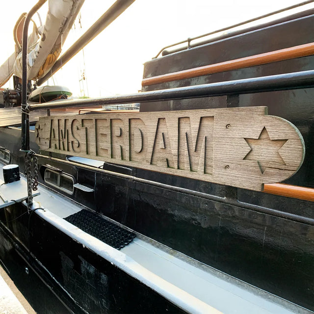 Wooden sign with ‘Amsterdam’ engraved on a boat parked in a canal in Amsterdam