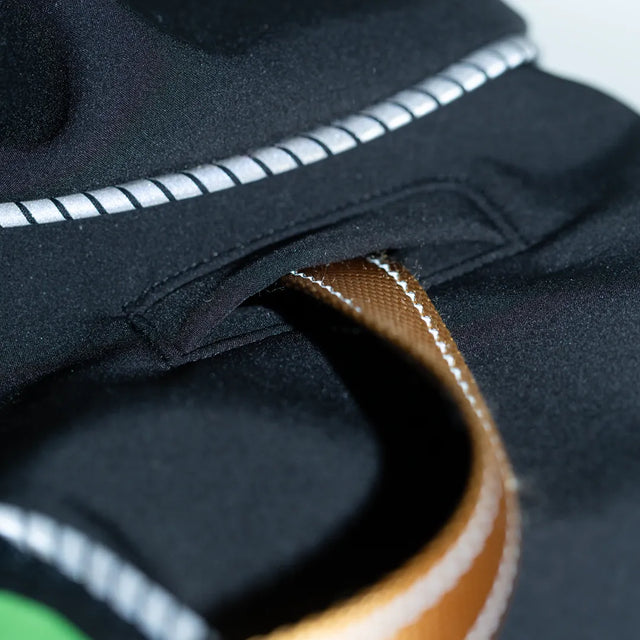 Closeup of a black modular dog raincoat leash hole with a light brown leash threaded through it, showing reflective piping between the body and hood
